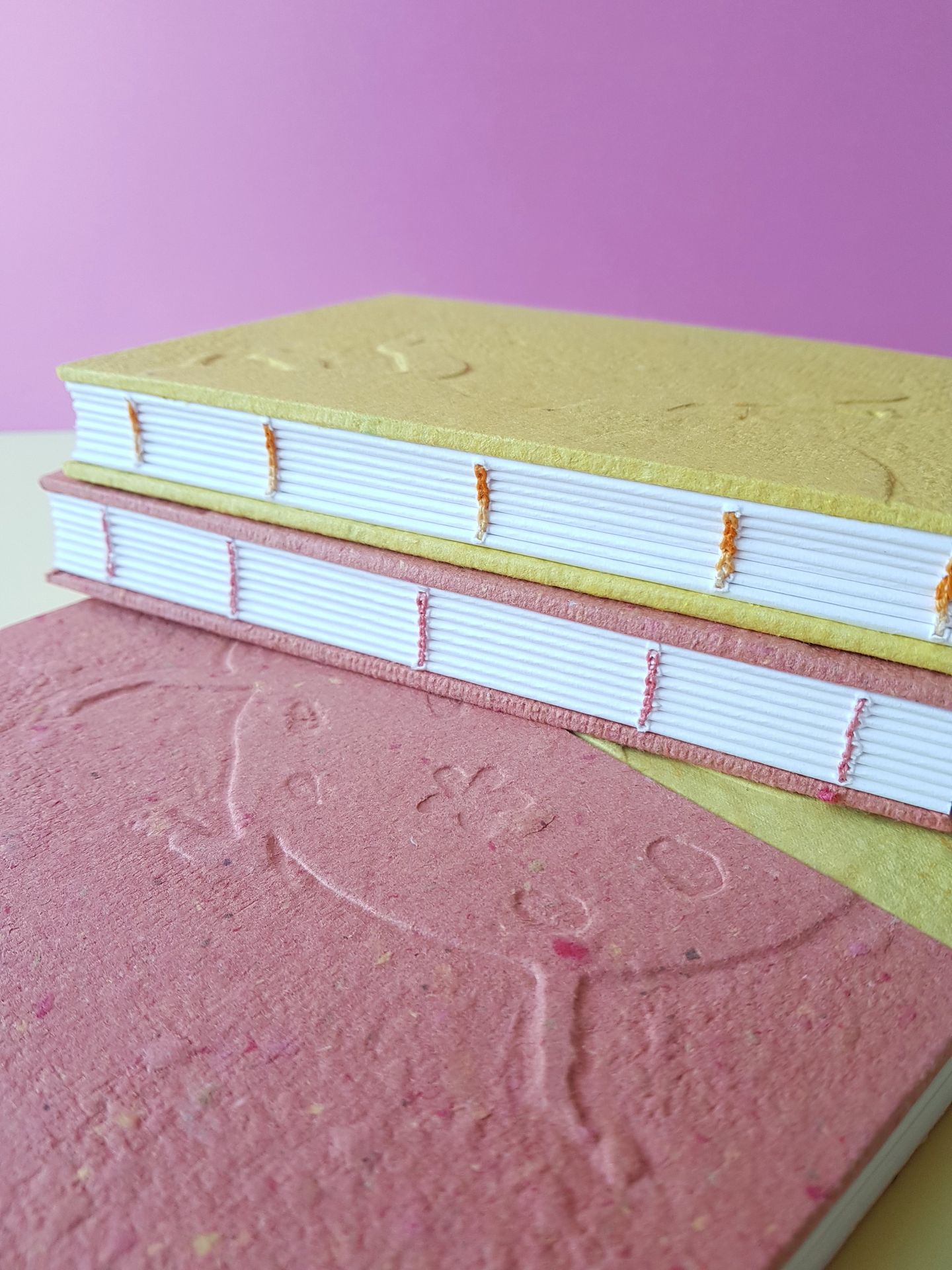 Carnets embossés de la collection "insecte" Détail d'une reliure copte sur deux carnets au couverture solide jaune et rose. Au premier plan, un carnet embossé au motif d'une coccinelle avec des tâches en formes de fleurs.