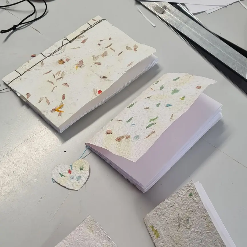 Carnets avec une couverture en papier recyclé avec inclusion végétale relié lors d'un atelier.
